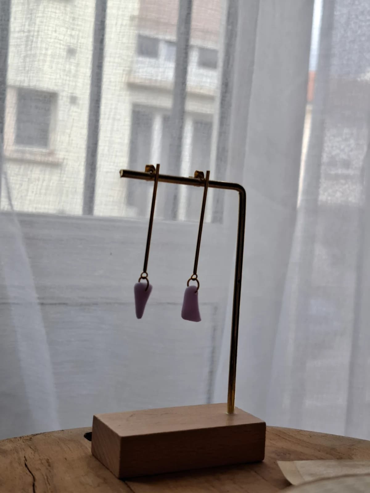 Boucles d'oreilles pendantes avec pendentifs violets suspendues sur un présentoir métallique.