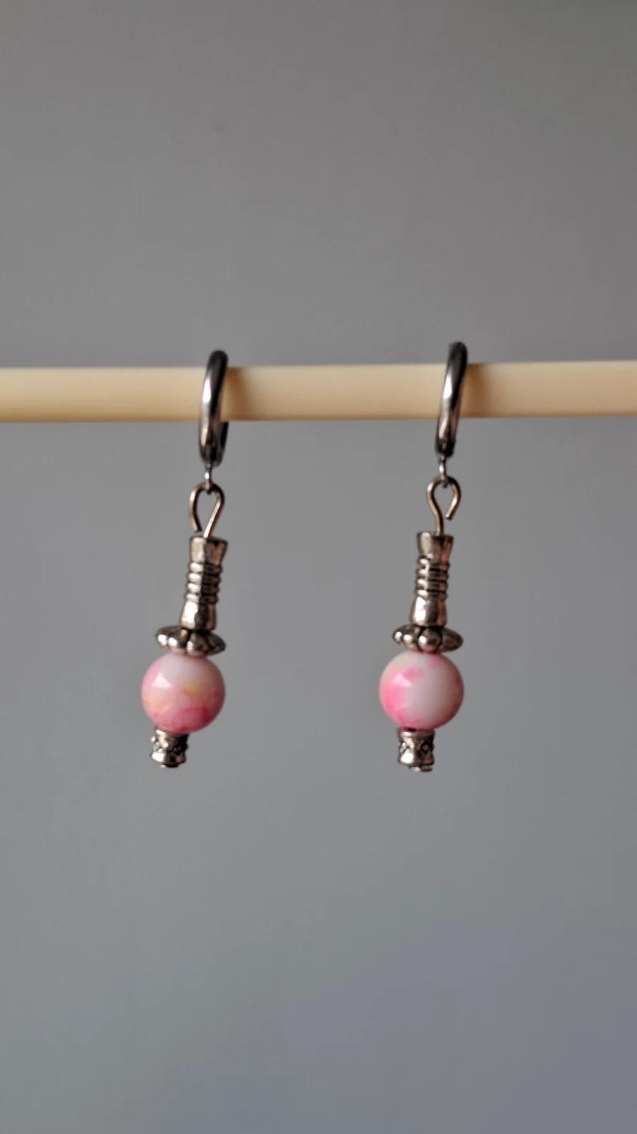 Boucles d'oreilles pendantes roses et argentées posées sur un disque de bois brut.
