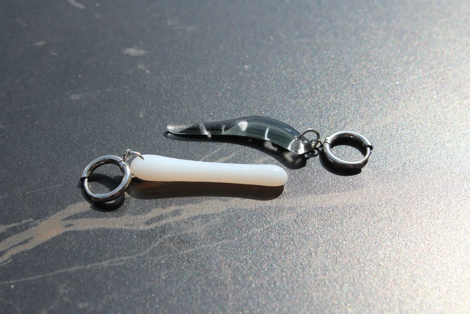 Paire de boucles d'oreilles asymétriques en verre noir et blanc avec anneaux en acier posées à plat.