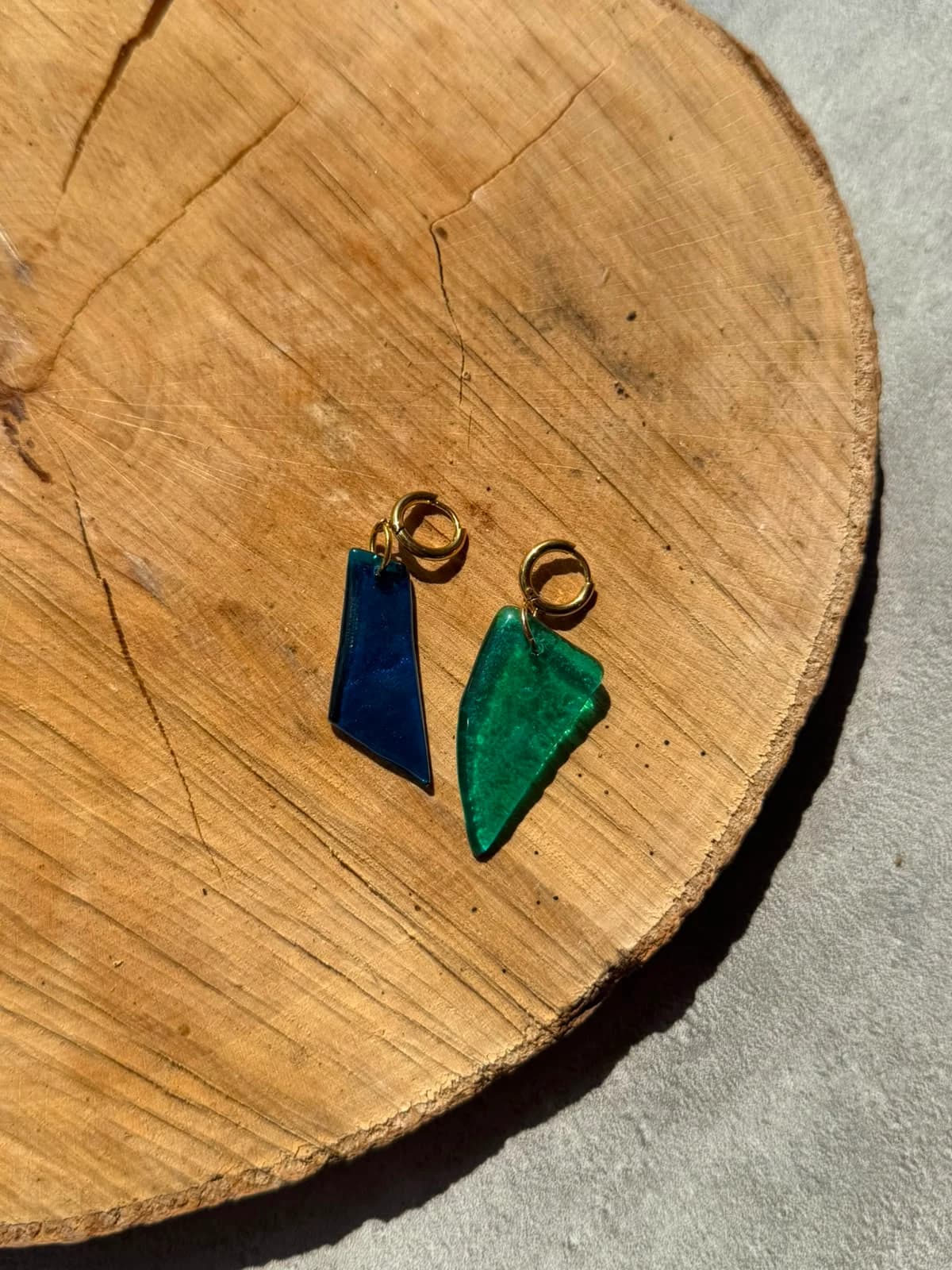 Paire de boucles d'oreilles en verre bleu roi et turquoise posée à plat sur un support en bois.