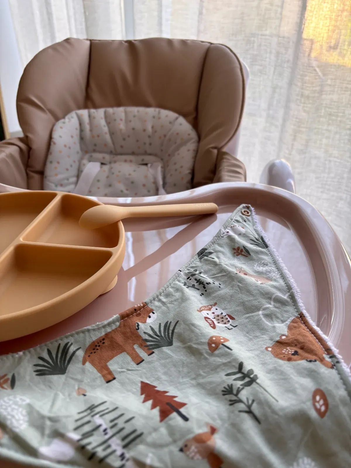 Gros plan sur le bavoir bandana déplié à motifs de forêt, à côté d'une assiette compartimentée.