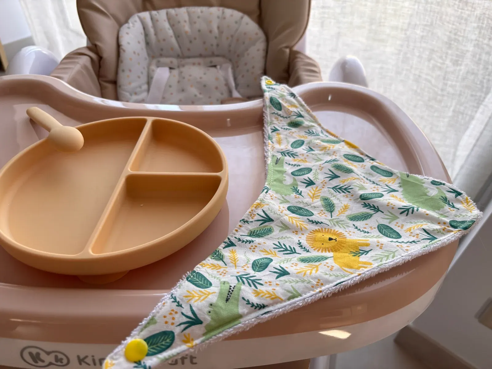 Bavoir bandana déplié à motifs tropicaux avec bouton pression jaune près d'une assiette pour bébé
