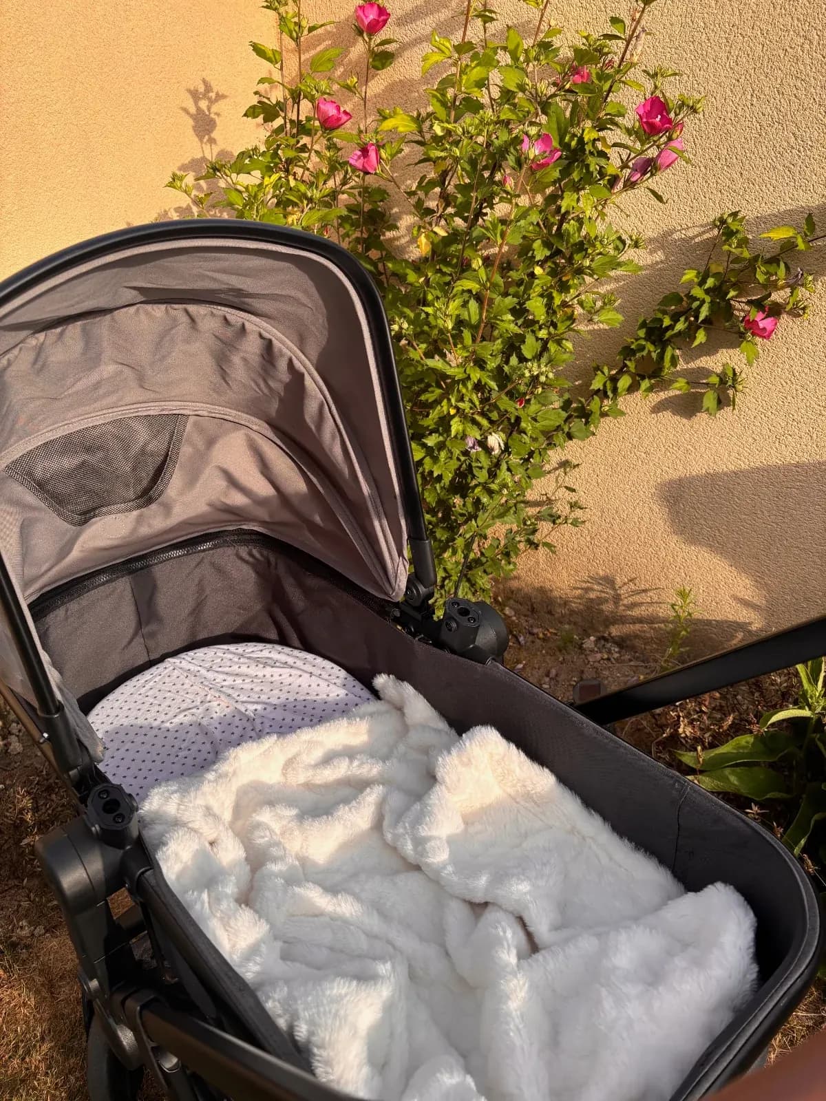 Couverture moelleuse blanche pour bébé disposée à l'intérieur d'une poussette noire en extérieur.