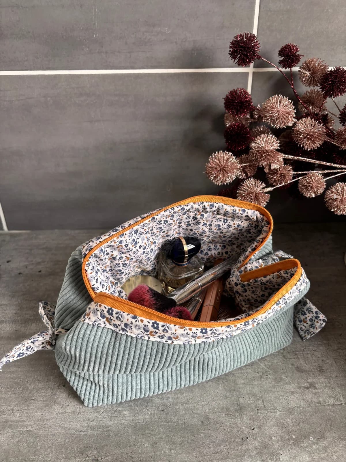 Trousse de toilette ouverte dévoilant sa doublure fleurie et remplie de cosmétiques et d'un flacon