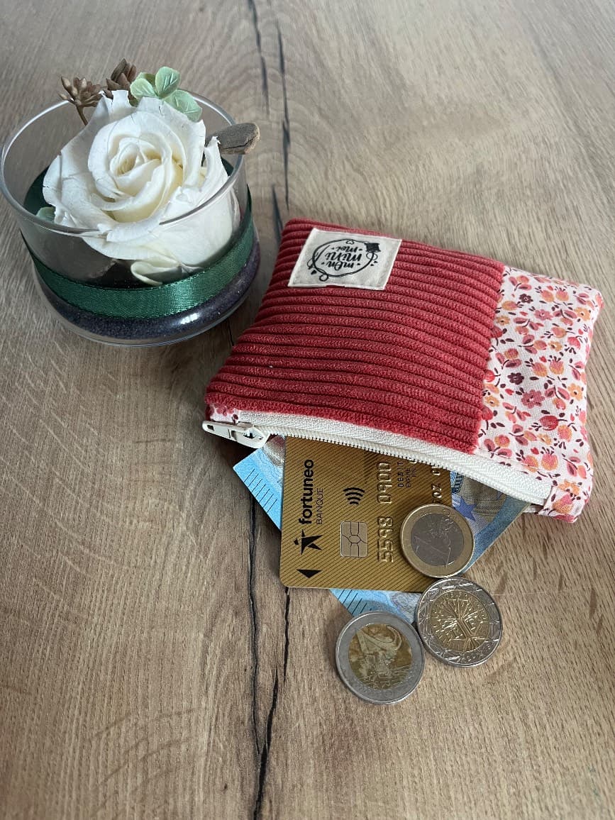 Pochette en velours rose et tissu fleuri entrouverte laissant voir de la monnaie et une carte.