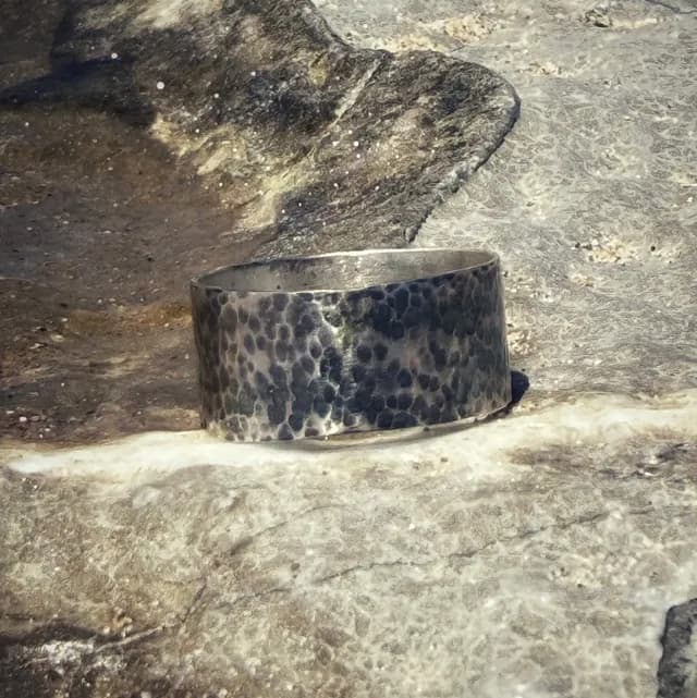 Vue de profil d'un anneau large martelé et patiné, posé à plat sur un support minéral.