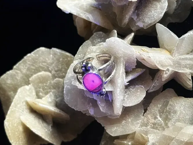 Bague en argent avec pierre centrale fluorescente rose vif sous lumière UV.