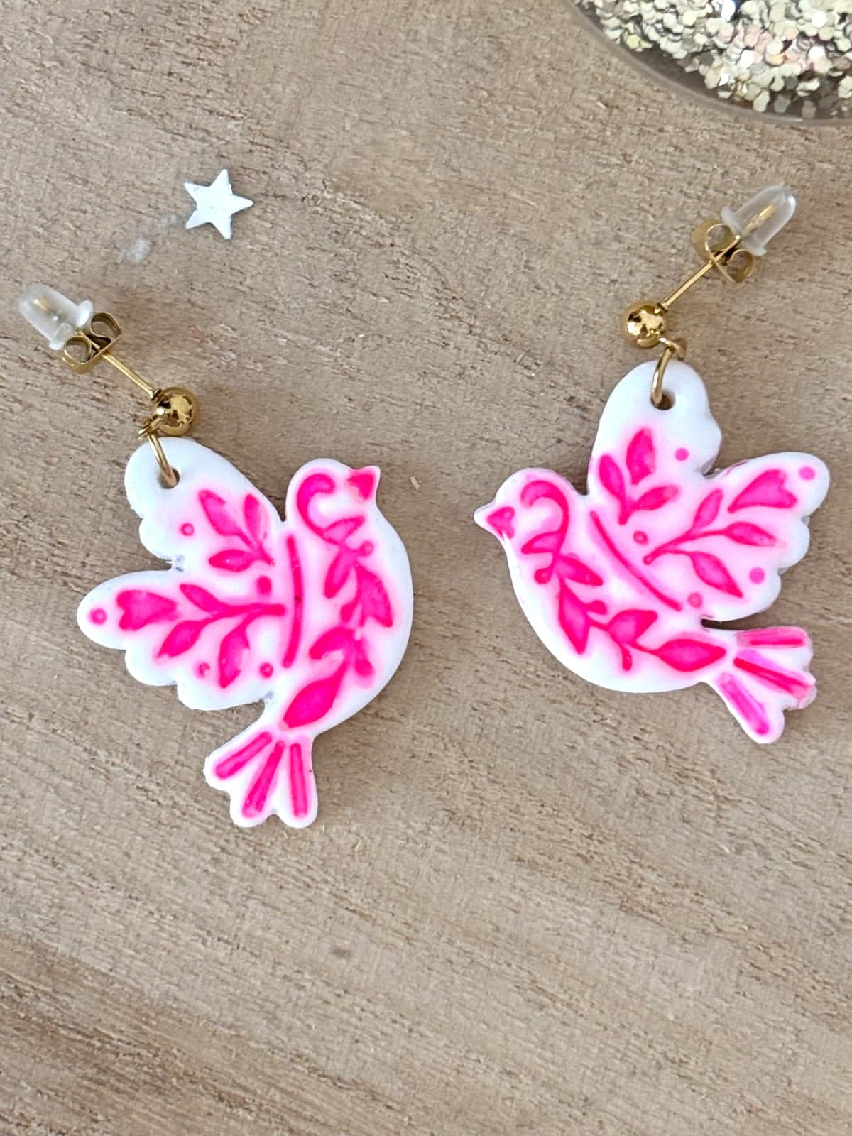 Gros plan sur les boucles d'oreilles oiseaux blancs ornées de motifs végétaux rose fluo.