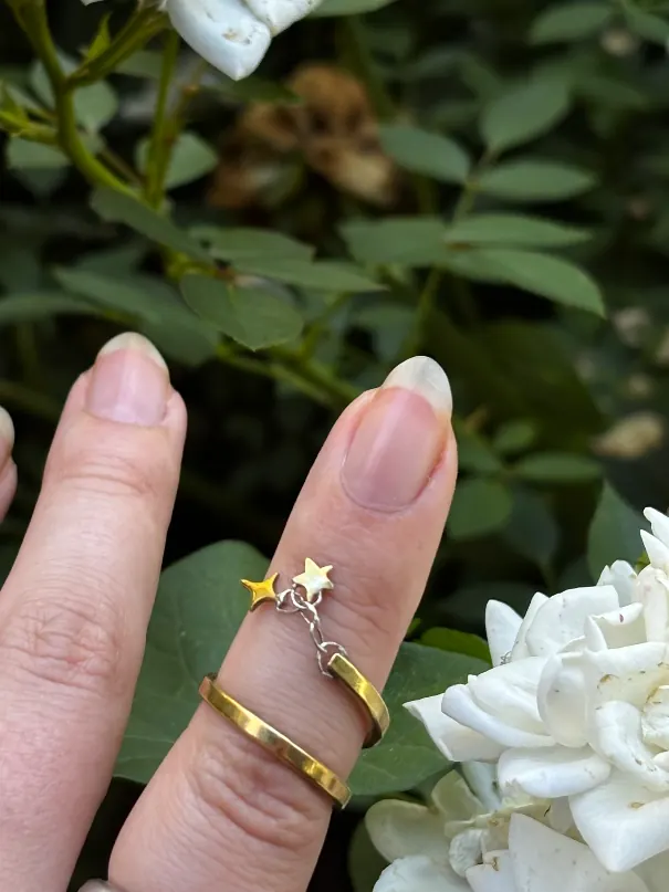 Bague spirale dorée à breloque étoiles portée devant des roses blanches