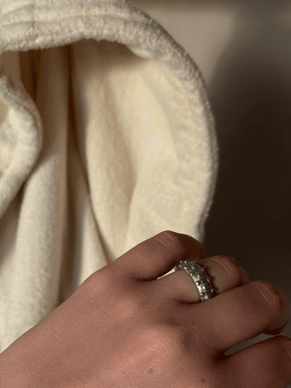 Bague argentée ornée de motifs de bulles portée à la main devant un tissu écru